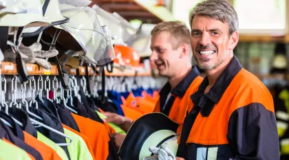 Zwei Feuerwehrleute in Schutzkleidung bereiten sich in einer Umkleide auf ihren Einsatz vor.
